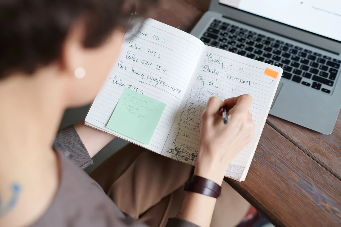 Person writing application notes in a notebook beside a laptop at a desk.