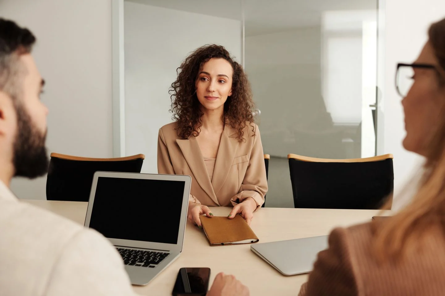 Job candidate listening to two interviewers across a table in a bright office.